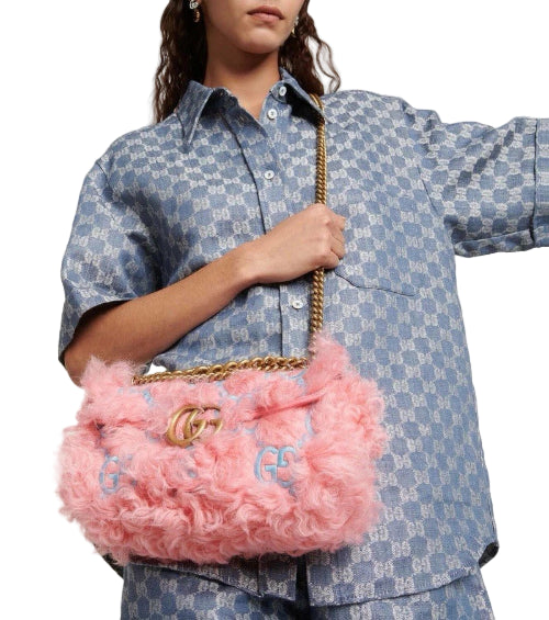 Person holding a pink fluffy handbag with gold chain strap against a light gray background