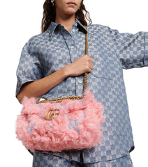 Person holding a pink fluffy handbag with gold chain strap against a light gray background