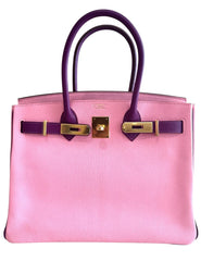 Pink handbag with purple handles and gold hardware on a white background