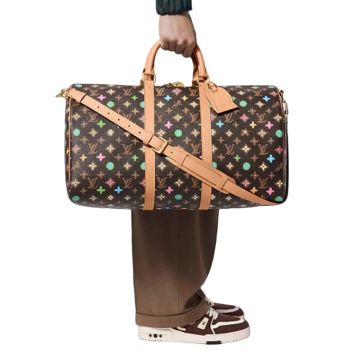 Patterned suitcase with brown straps held by a person wearing brown pants and shoes on a black background