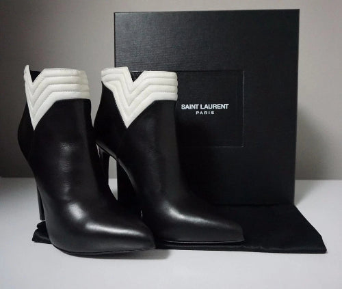 Black high-heeled boots with white trim in front of a Saint Laurent box.