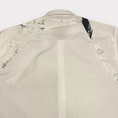 Close-up back view of a cream-colored shirt with black speckled and striped patterned detailing on the shoulders and upper back.