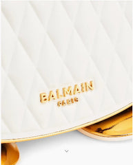 Close-up of a white quilted Balmain Paris handbag with gold lettering and a gold metallic trim, showing the brand logo clearly.