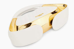 A white and gold metallic visor-style headband or mask with a glossy reflective finish, shown on a plain light gray background. The brand name 'BLOOMBERG' is printed in gold on the white inner surface.