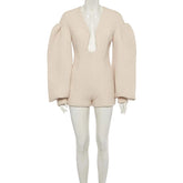 A light beige textured knit romper with dramatic puffed balloon sleeves and a deep plunging neckline, displayed on a white mannequin against a light gray background.