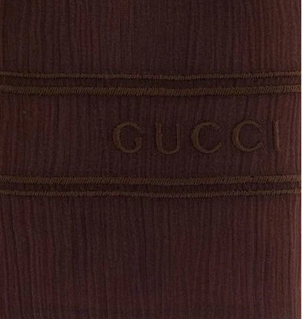 Close-up of a dark brown ribbed knit fabric with horizontal stitched bands and the embossed brand name GUCCI across the center.