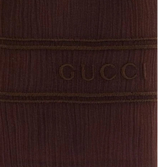 Close-up of a dark brown ribbed knit fabric with horizontal stitched bands and the embossed brand name GUCCI across the center.
