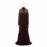 A dark brown long-sleeved maxi dress with a sheer mesh high-neck overlay and a pleated skirt, displayed on a white mannequin against a plain white background.