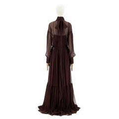 A dark brown long-sleeved maxi dress with a sheer high-neck overlay and a tie at the collar, displayed on a mannequin against a white background.
