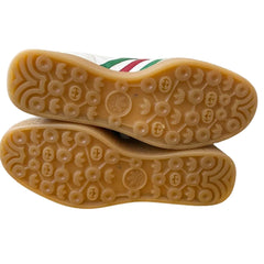 The soles of a pair of white leather sneakers with green and red stripes, showing a tan gum rubber bottom with circular tread patterns.