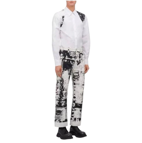 A model wearing a white long-sleeve shirt with black shoulder patches and black-and-white patterned trousers, standing against a plain white background.