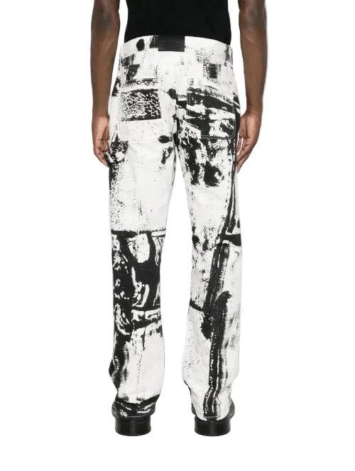 A person shown from the back wearing wide-leg trousers with an abstract black and white paint-splatter print, paired with a black top and black shoes, against a plain white studio background.