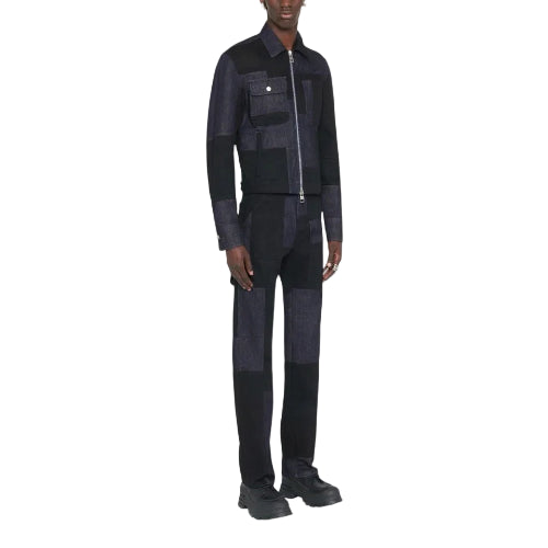 A model wearing a dark patchwork denim jacket and matching pants with a silver zipper, photographed against a light gray studio background.