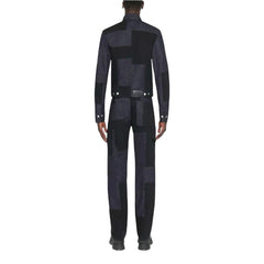 A model shown from the back wearing a dark patchwork suit with a high collar, long sleeves, and a matching belt, set against a solid light gray background.