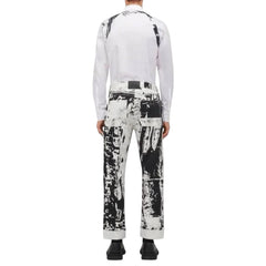 A model shown from the back wearing a white long-sleeve shirt and black-and-white abstract print trousers, paired with black shoes, against a light gray background.
