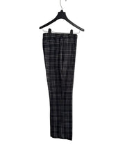 Black and white plaid cropped pants hanging on a black hanger against a white paneled door.