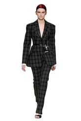 A model walks down a runway wearing a black and white plaid blazer and matching trousers, styled with a small black crossbody bag and a red headband.