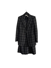 A black and white plaid blazer and matching skirt set hanging on a black hanger against a white paneled door.