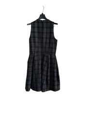 A sleeveless black and white plaid dress hanging on a black hanger against a white paneled door.
