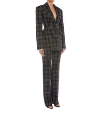 A model wearing a black and white plaid two-piece suit with a structured blazer and matching wide-leg trousers, styled with black strappy heels against a light gray studio background.