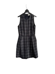 A sleeveless black and gray plaid dress hanging on a black hanger against a white paneled door.