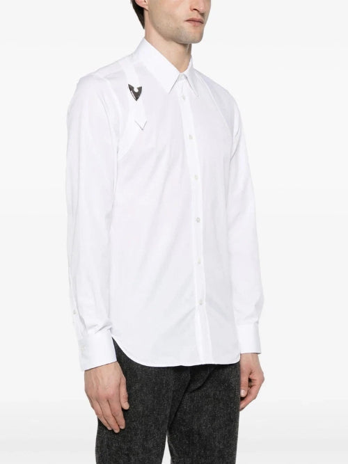 A man wearing a white long-sleeve button-down shirt with a small embroidered logo on the chest, paired with black trousers, shown against a plain white background.