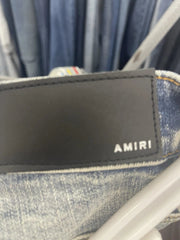 A black rectangular AMIR portable speaker with a glossy finish, resting on a gray textured fabric surface.