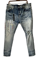Light blue distressed denim jeans with colorful thread-like embellishments on the left leg, hanging on a wooden hanger against a plain white wall.