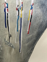 Close-up of a gray denim fabric with multiple vertical embroidered or painted streaks in blue, white, red, yellow, and black.