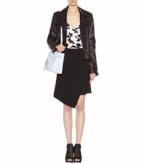 Person wearing a brown leather jacket, floral top, and black skirt holding a white bag on a white background