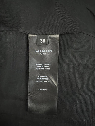 Close-up of a black Balmain Paris garment tag labeled size 38, sewn inside a black textured fabric garment.