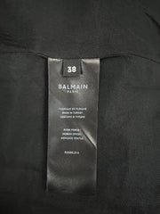 Close-up of a black Balmain Paris garment tag labeled size 38, sewn inside a black textured fabric garment.
