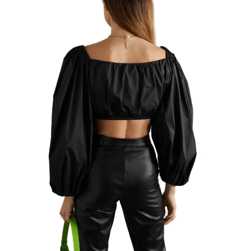 Person wearing a black off-shoulder top and black leather pants against a plain background