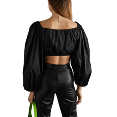 Person wearing a black off-shoulder top and black leather pants against a plain background