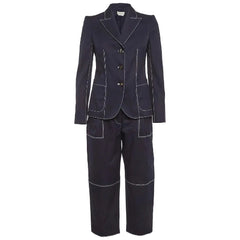 A dark navy blue two-piece suit with contrasting light gray piping details, featuring a double-breasted blazer and matching trousers, shown against a light gray background.
