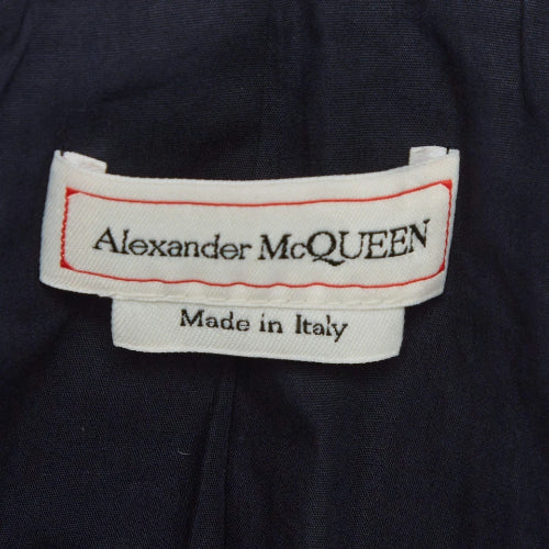 Close-up of a dark navy fabric garment showing two white brand labels. The top label reads 'Alexander McQUEEN' with a red stitched border, and the bottom label reads 'Made in Italy'.