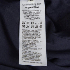 A close-up of a white garment care label for Alexander McQueen, showing the brand name and washing instructions printed in black text on a dark navy or black fabric background.