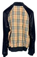 A vintage Burberry-style plaid jacket with black satin sleeves and collar, featuring a beige plaid body with red and navy check lines, hanging on a black hanger against a white door.