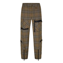 A pair of plaid trousers in a brown, beige, and black tartan pattern, featuring black cargo pockets with zippers and black drawstring details at the ankles, shown against a light gray background.