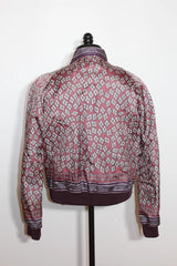 A long-sleeve patterned jacket displayed on a black dress form mannequin against a plain white wall. The jacket features a geometric diamond pattern in dusty pink, white, and dark purple, with a solid dark purple ribbed hem and cuffs.