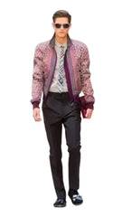 A male model walks down a runway wearing a patterned pink and purple bomber jacket over a patterned shirt, paired with black trousers and loafers.