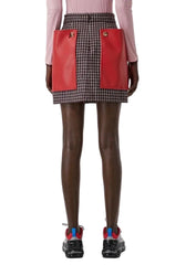 A model from the back wearing a red and black pleated skirt with two large front patch pockets, paired with brown tights and black sneakers.