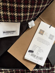 Close-up of a Burberry garment showing the interior label, hangtag, brown paper packaging, and a tartan pattern in burgundy, beige, and black.