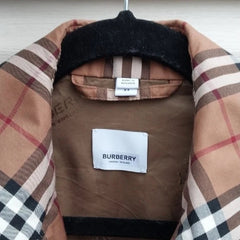 A Burberry check coat draped over a black hanger, showing a brown and beige plaid pattern with a white Burberry label in the center.