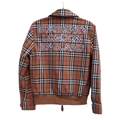 A brown and beige plaid jacket with a colorful geometric pattern across the chest, hanging on a white slatted wall.