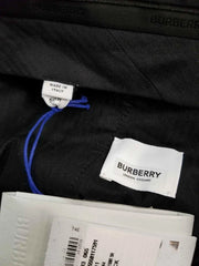 Close-up of a black Burberry garment interior showing a white Burberry London England label, a small 'Made in Italy' tag with a blue string, and white retail tags at the bottom.