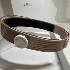 Brown Christian Dior belt with a silver buckle on a white surface.