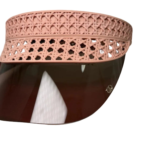 A close-up of a light pink woven or crocheted visor hat resting on a white surface, with part of a brown leather item visible underneath.