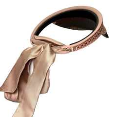 A blush pink woven headband with a matching satin ribbon bow, displayed on top of a white Dior box.