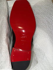 A close-up of a red and black shoe sole, showing a glossy red heel counter and black midsole, photographed against a white textured background.